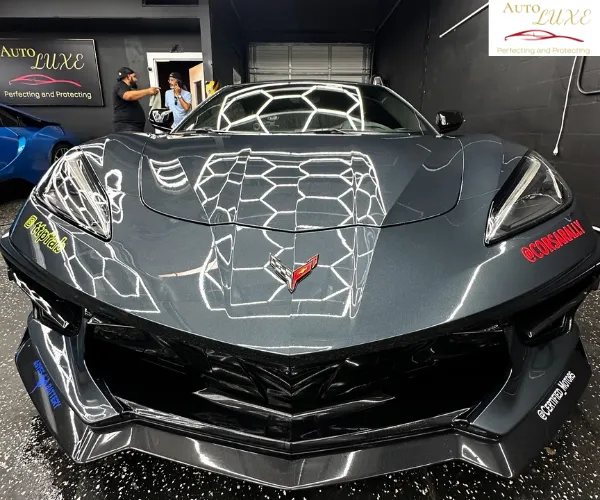 A front-facing view of the same dark gray sports car, highlighting the reflective surface of the hood and aggressive front splitter under studio lights.