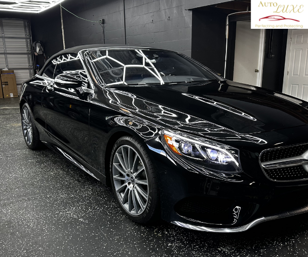 A side profile view of the luxury sedan, showcasing the clean, seamless application of dark window tint across both side windows under bright overhead workshop lighting.