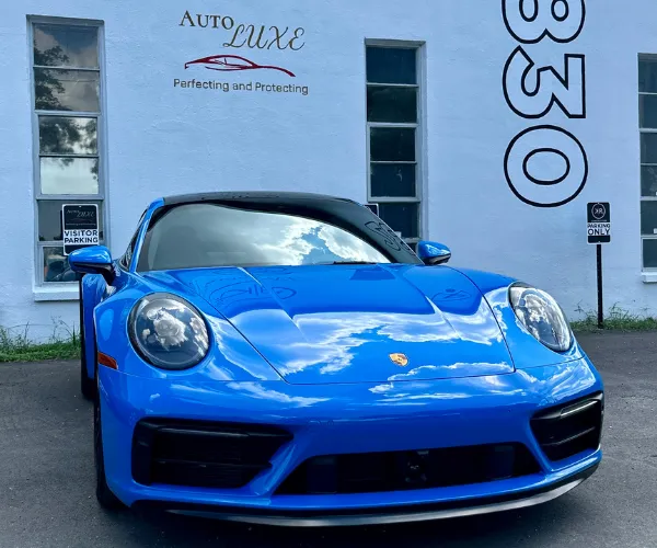 A front three-quarter angle of the polished blue sports car displaying high-gloss paint and clear sky reflections on its body panels, referencing paint correction.