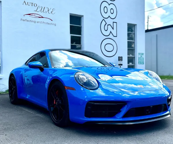 A front three-quarter angle of the polished blue sports car displaying high-gloss paint and clear sky reflections on its body panels, referencing paint correction.